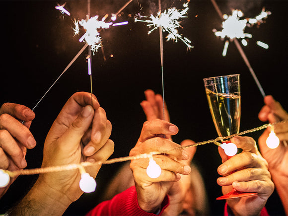 Hände die auf einer Silvesterparty mit Sekt und Wunderkerzen auf das neue Jahr anstoßen