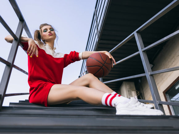 Sportliche, große Frau mit langen Beinen sitzt mit einem Basketball in der Hand auf einer Treppe